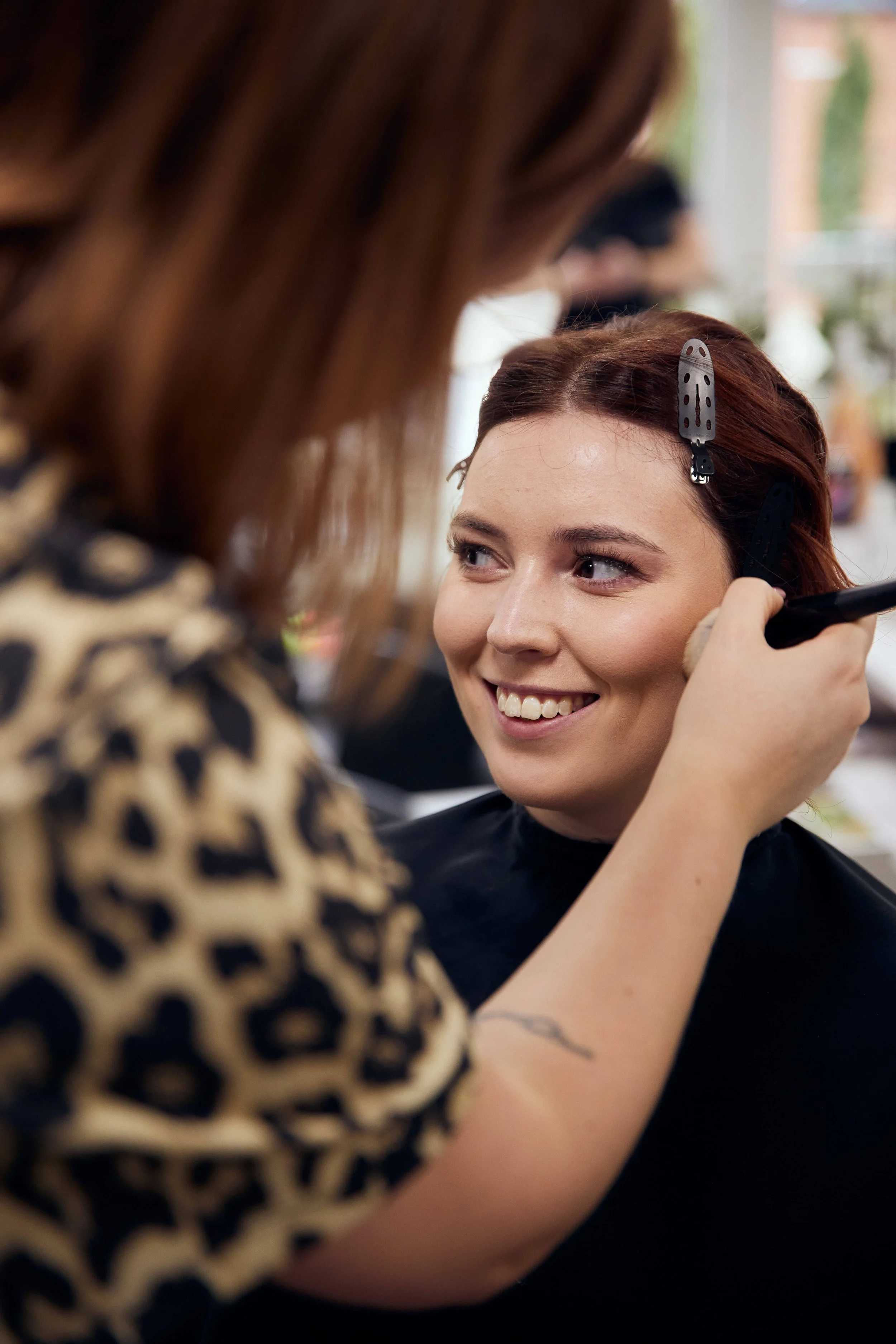 Stylist udfører finjustering af makeup på brud i rolige og lyse omgivelser, fokus på nærvær og detaljer."