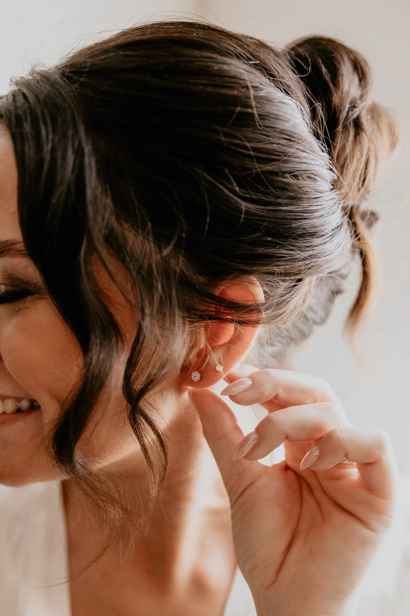 Detaljebillede af brud, der sætter ørering i – naturligt lys, bløde toner og elegant brudestyling af RiiStyle.