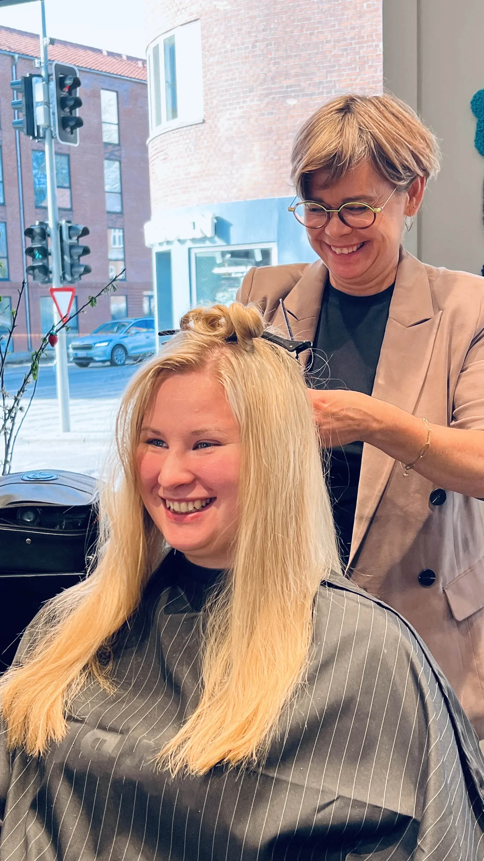 Smilende og glad frisør og brud som er igang med at forberede stylingen af brudehår og makeup på bryllupsdagen