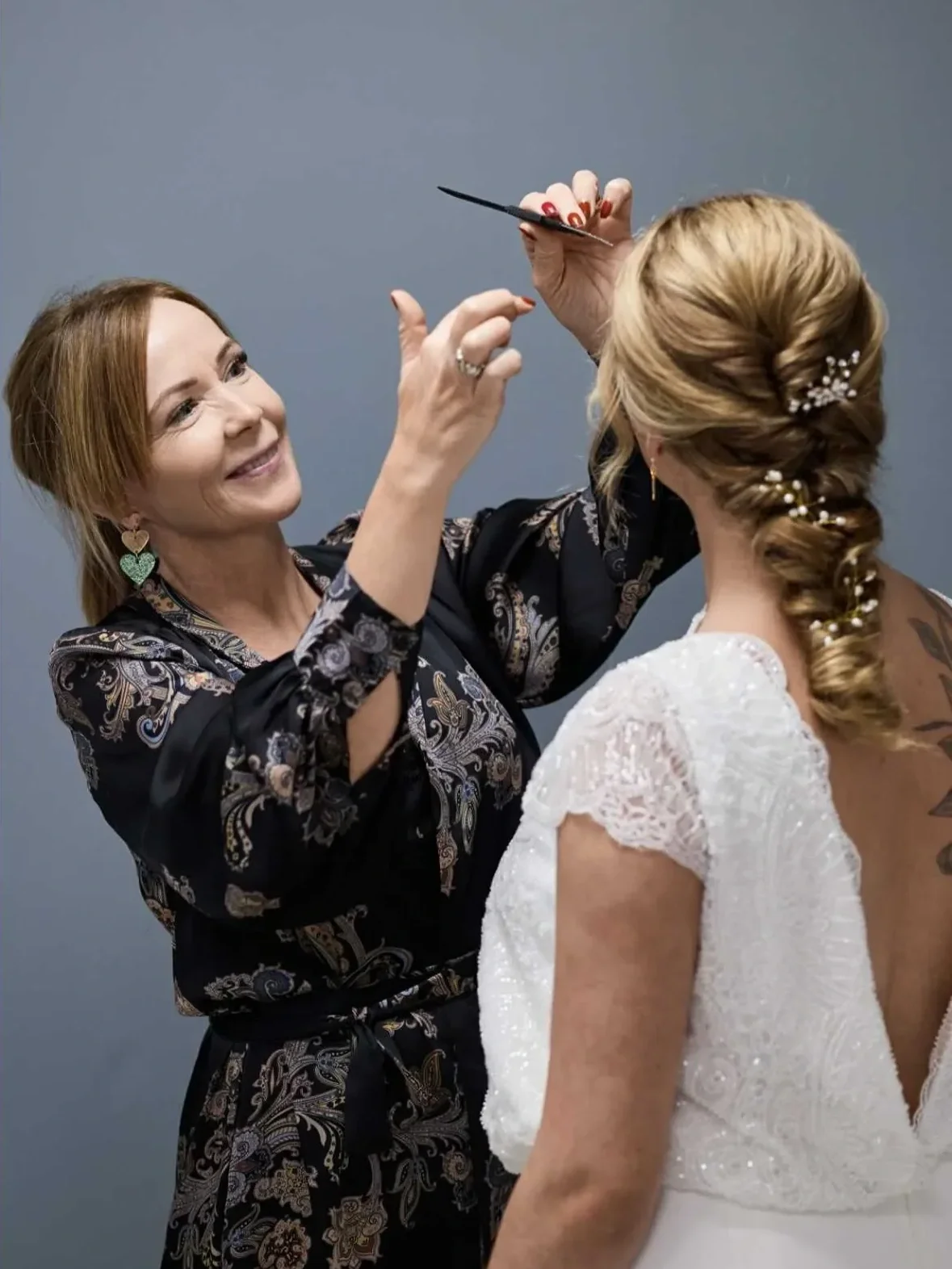 En brud i brudekjole med dyb rygudskæring står med ryggen til kamera imens frisøren retter de sidste detaljer på håret inden afgang til kirken