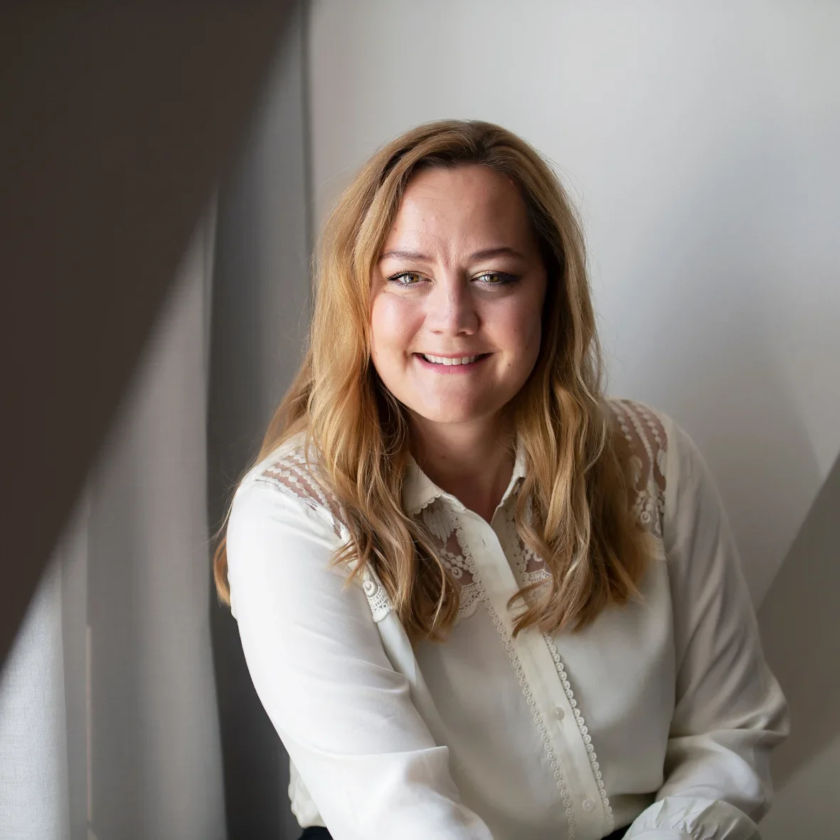 Rikke, grundlægger af RiiStyle, sidder smilende i blødt skandinavisk lys – portræt til Om RiiStyle-siden.