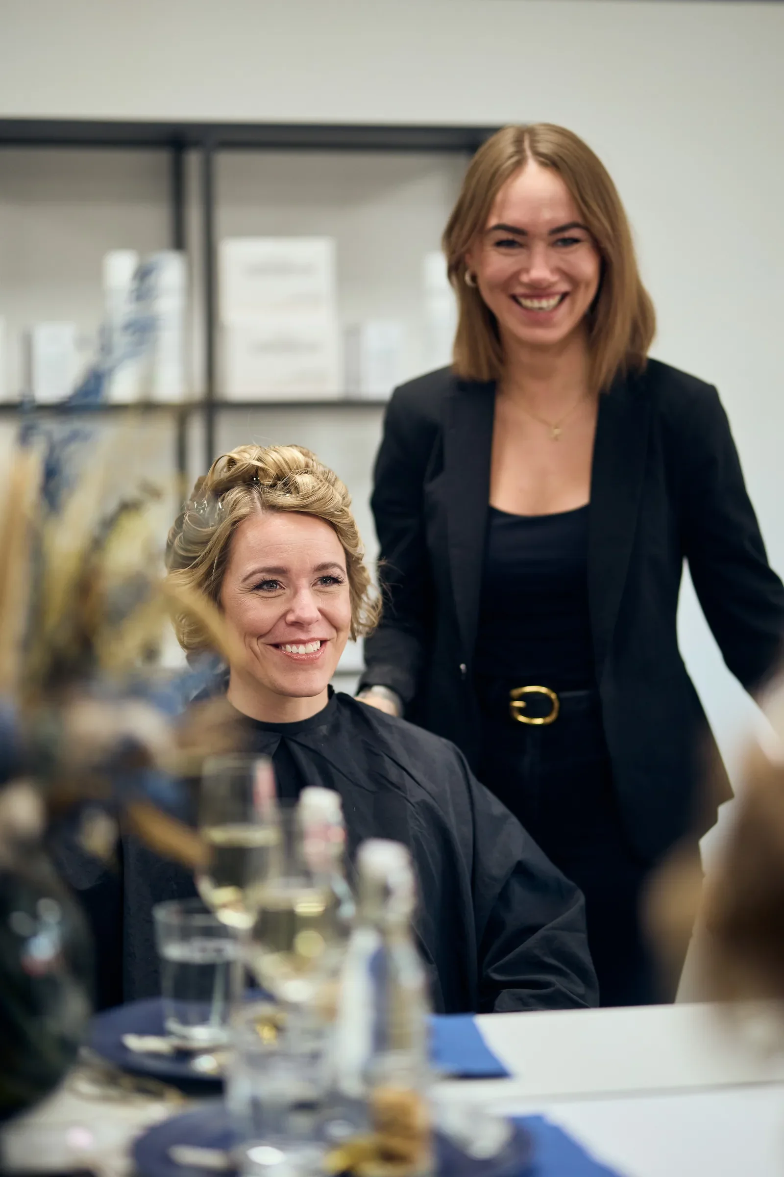 Glad brud sidder i stolen med curlere imens den smilende frisør står bagved stemningen er rolig og tryg