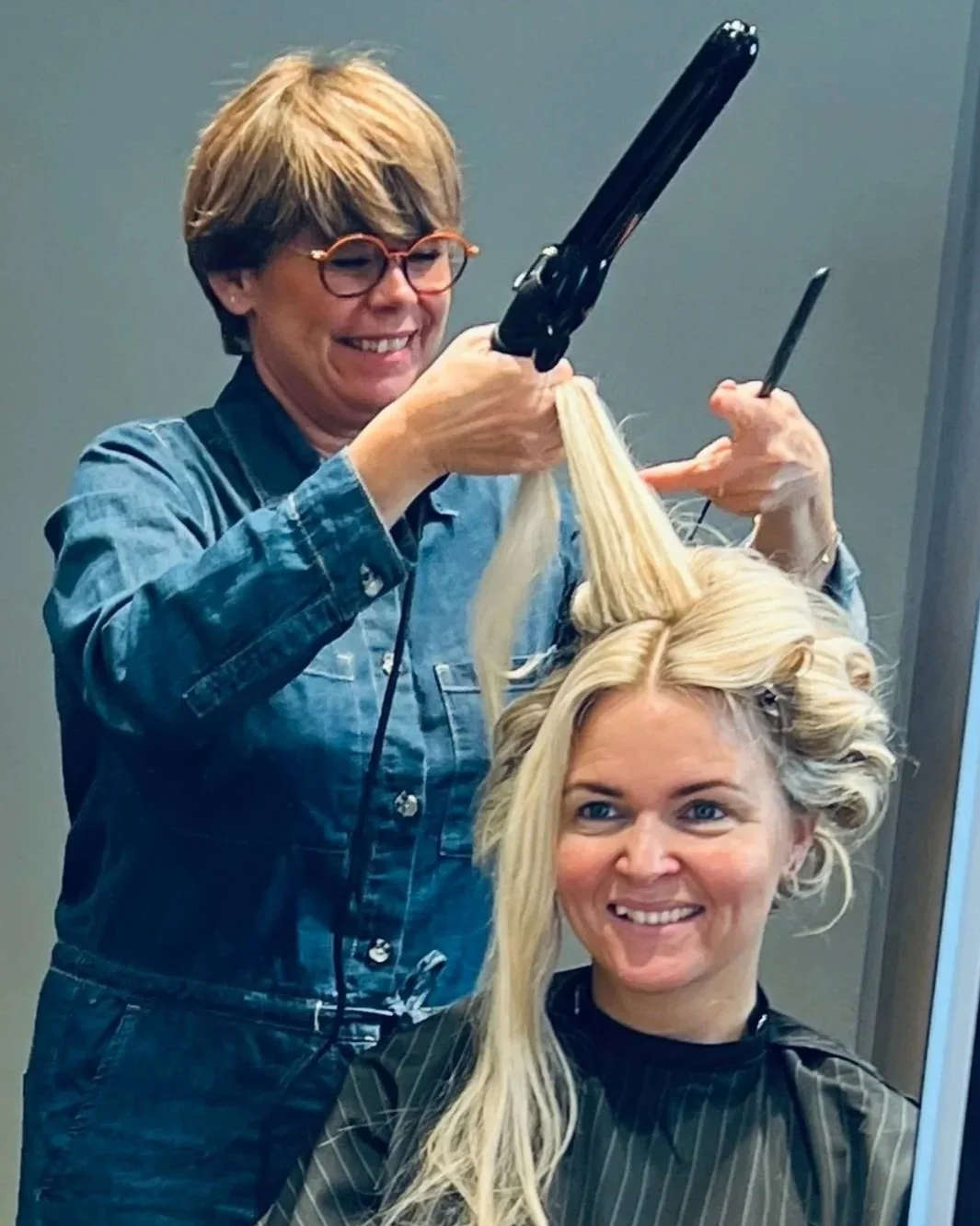 Blond brud sidder i stolen og får krøllet håret op til hendes bryllupsdag