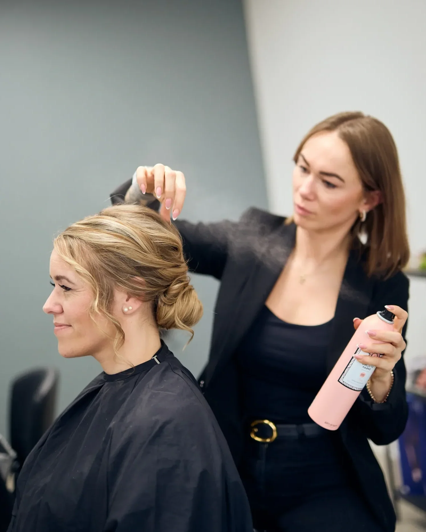 Frisør og brudestylist med hårspray i hånden fuldender de sidste detaljer på en romantisk og løs brudeopsætning