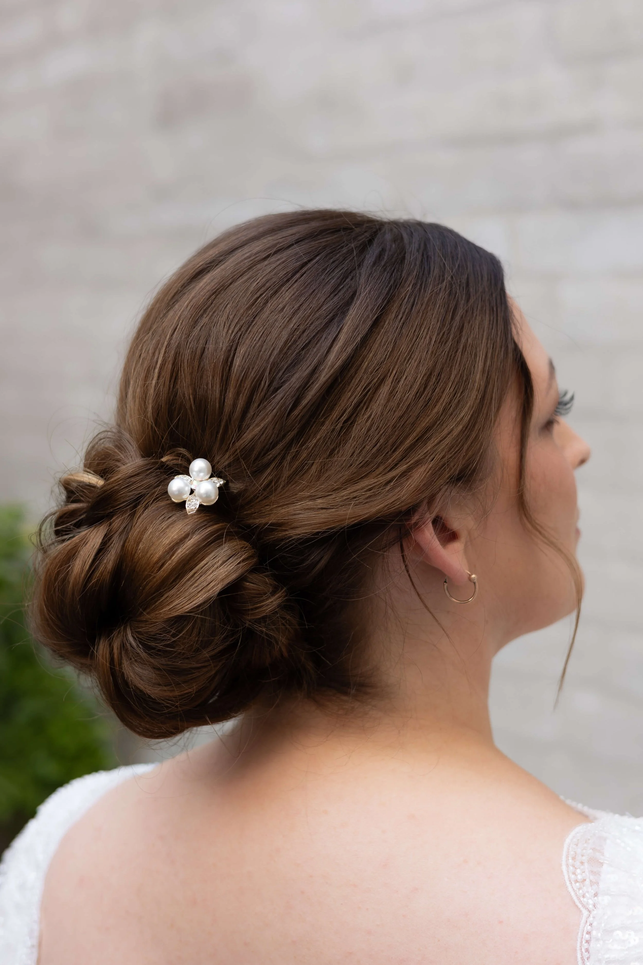 Elegant brudefrisure i lav knude med perledetaljer, fotograferet bagfra for at vise struktur og styling.