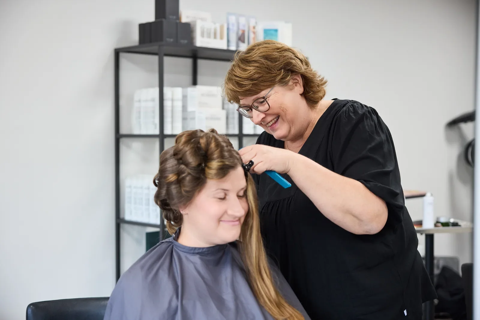 Frisør er igang med at forberede et kraftigt mørkt og langt hår hun smiler og har god stemning med sin kunde