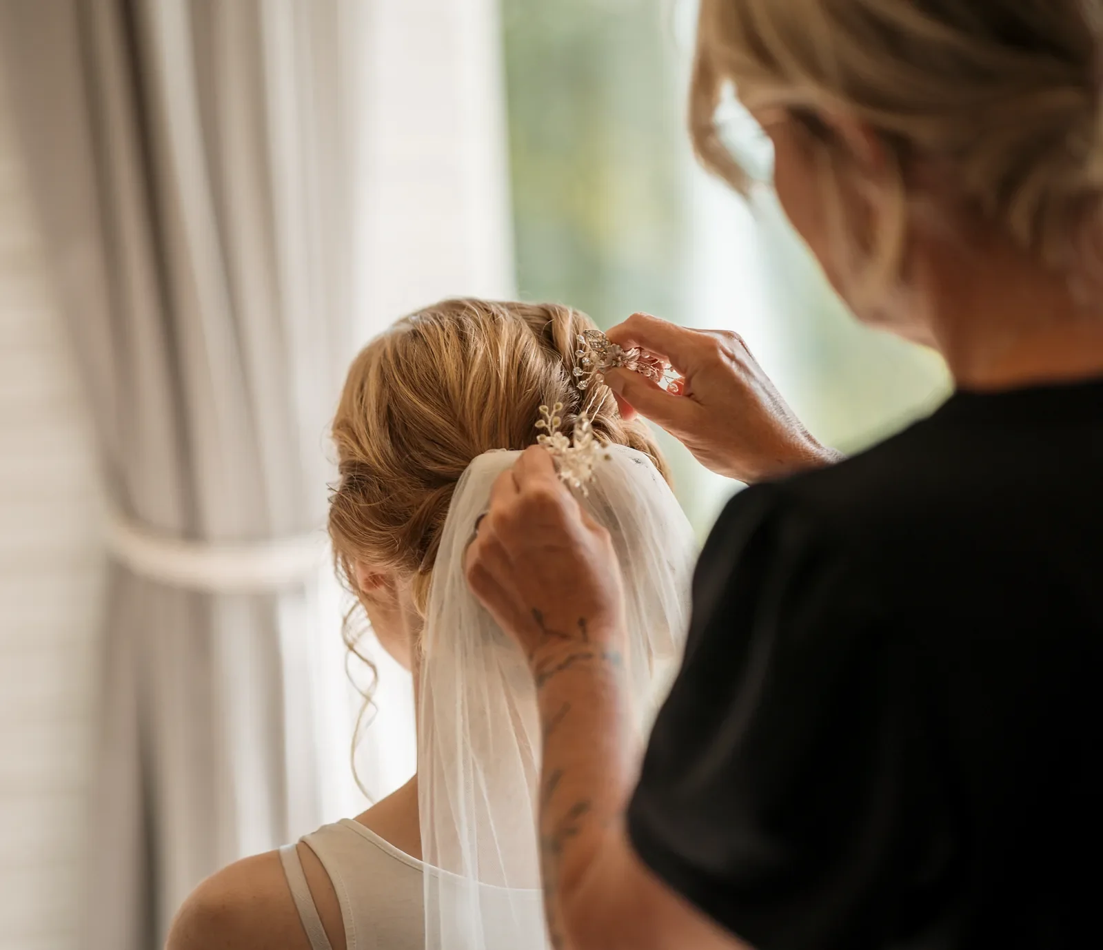 Lyst billede med frisørens hænder der sætter hårsmykke og slør i brudens hår