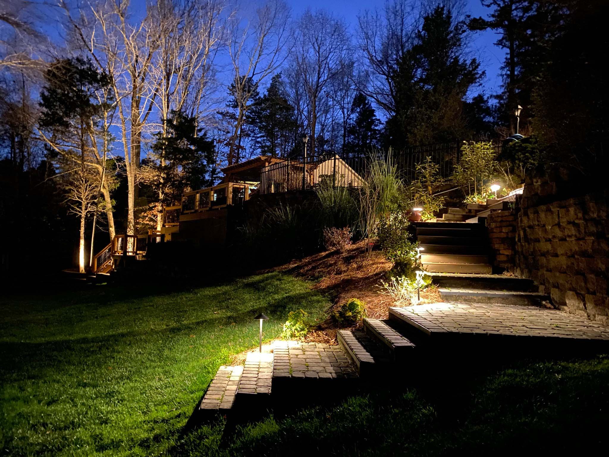  Steps leading from a raised patio down to a grassy yard illuminated with path lights.  