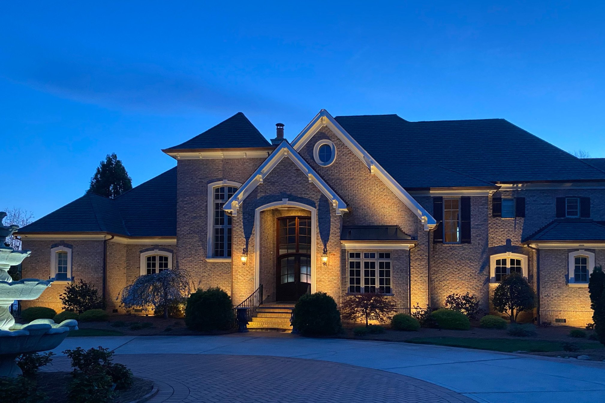  Large, light colored brick home with architectural up lighting and landscape lighting. 