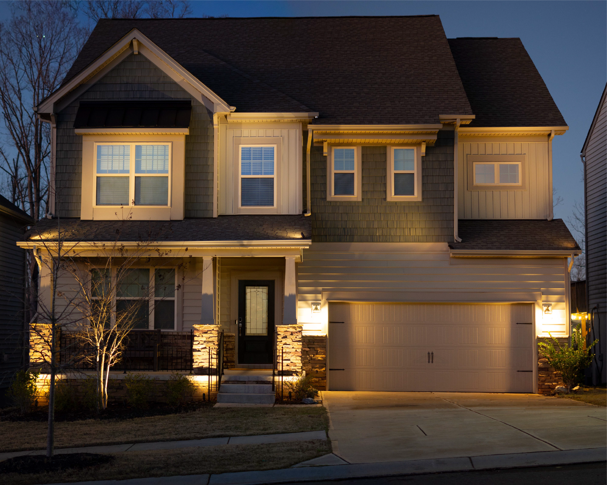  Green and tan craftsman style home illuminated with a combination of architectural up lights and landscape lighting. Small crepe myrtle with accent lights is positioned in front of the home. 