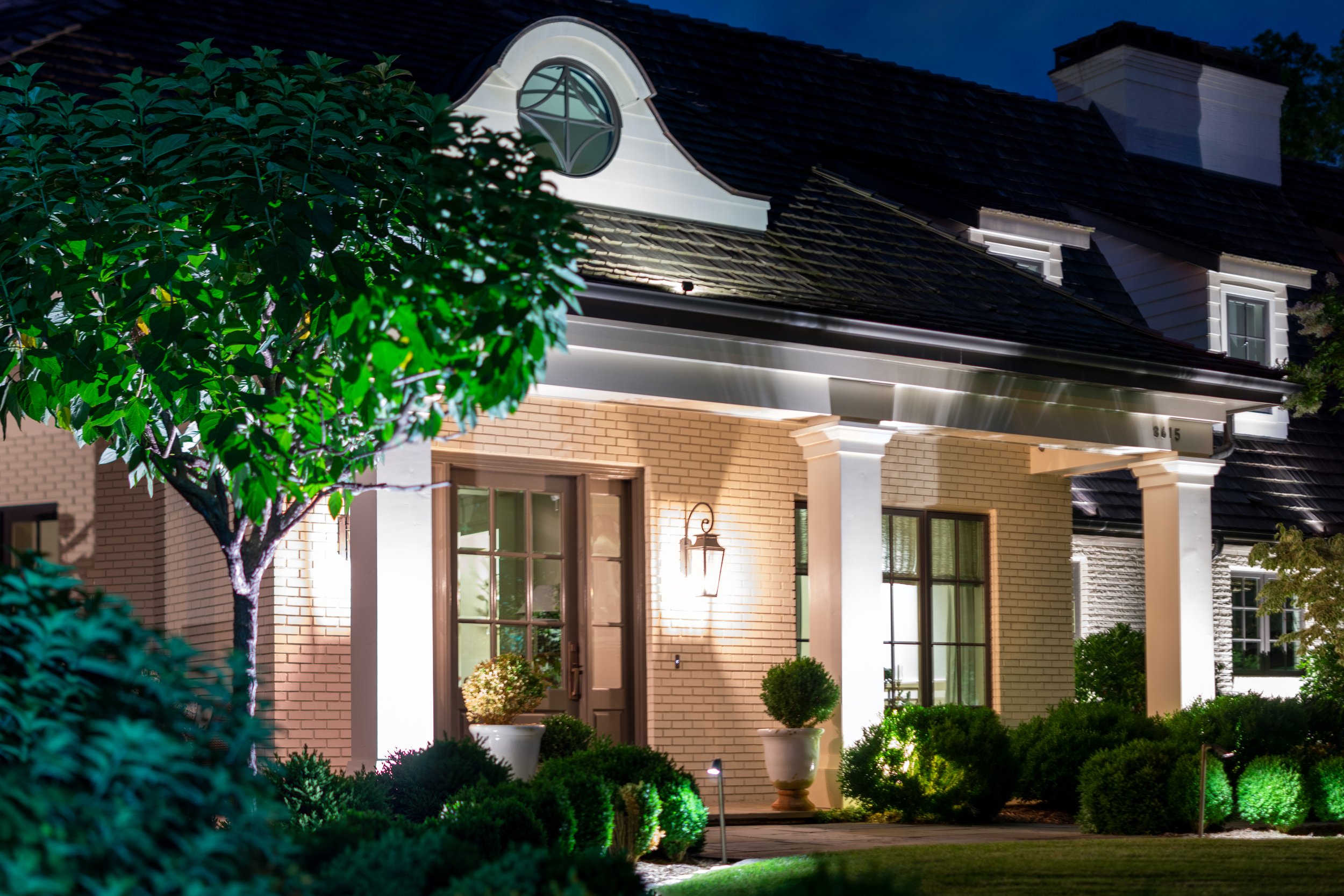  White brick home with large white columns is illuminated with a combination of architectural lighting and landscape lighting.  