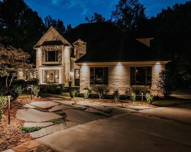  Tan stone and brick home is illuminated with downlights mounted in the soffits.  