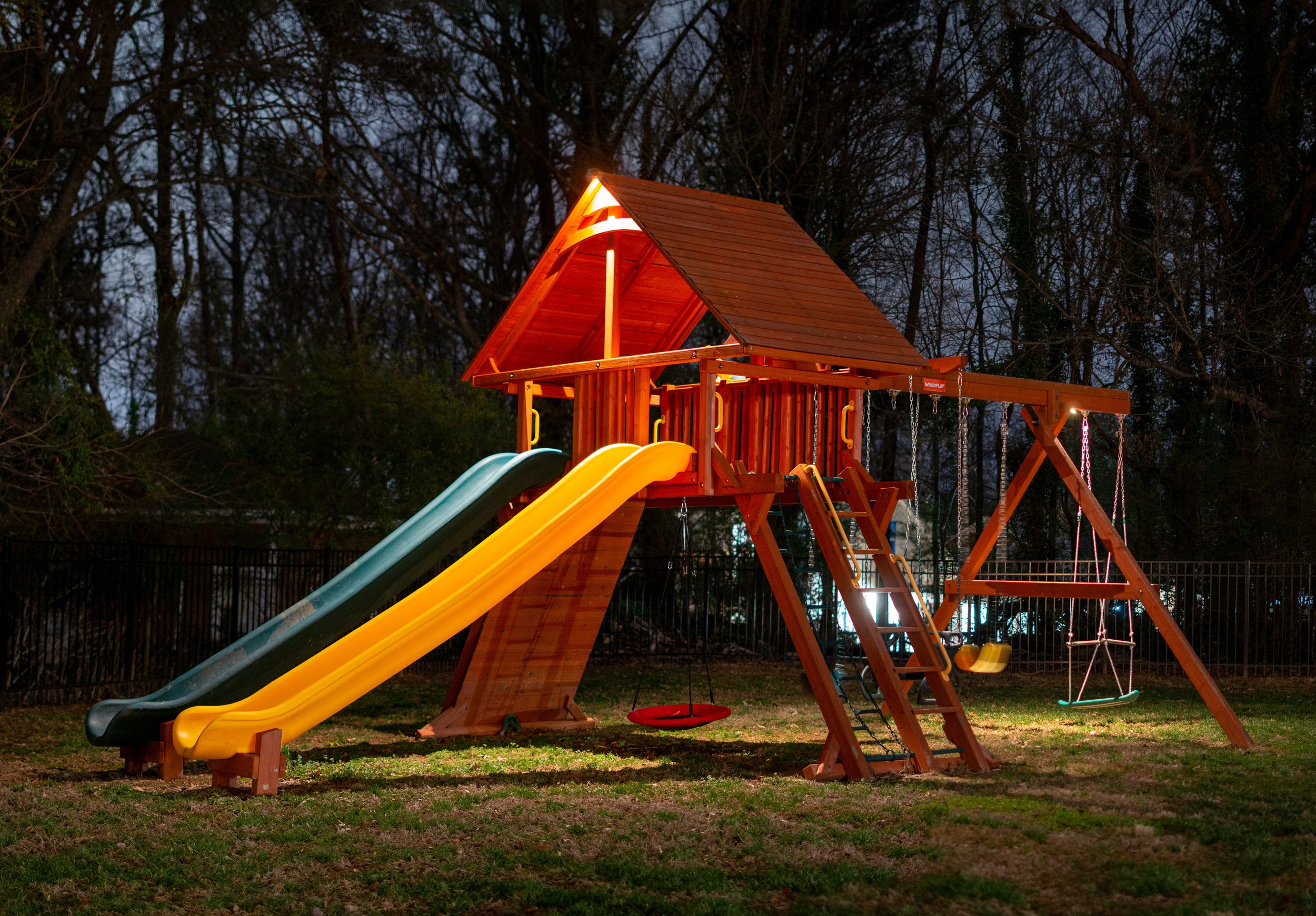  Playset with slides is illuminated with landscape lighting. A series of downlights are mounted in the peaks of the playset. 