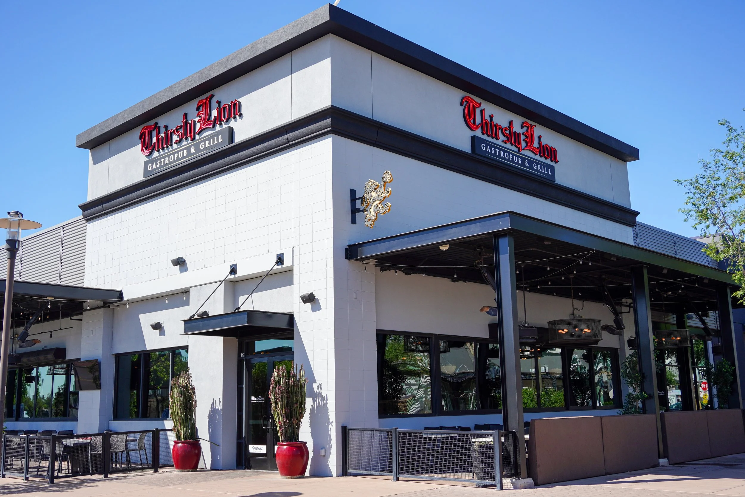 Exterior of Thirsty Lion SanTan, an Arizona restaurant with outdoor seating, potted plants, and a bright blue sky.