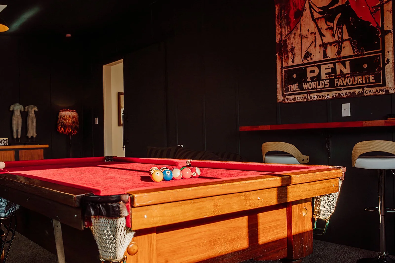 Indoor room with a pool table, billiard balls, chairs, and wall decorations including art pieces and a vintage poster.
