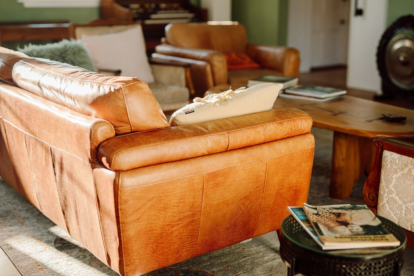 Living room with a leather sofa, a wooden coffee table, and various pillows and magazines.