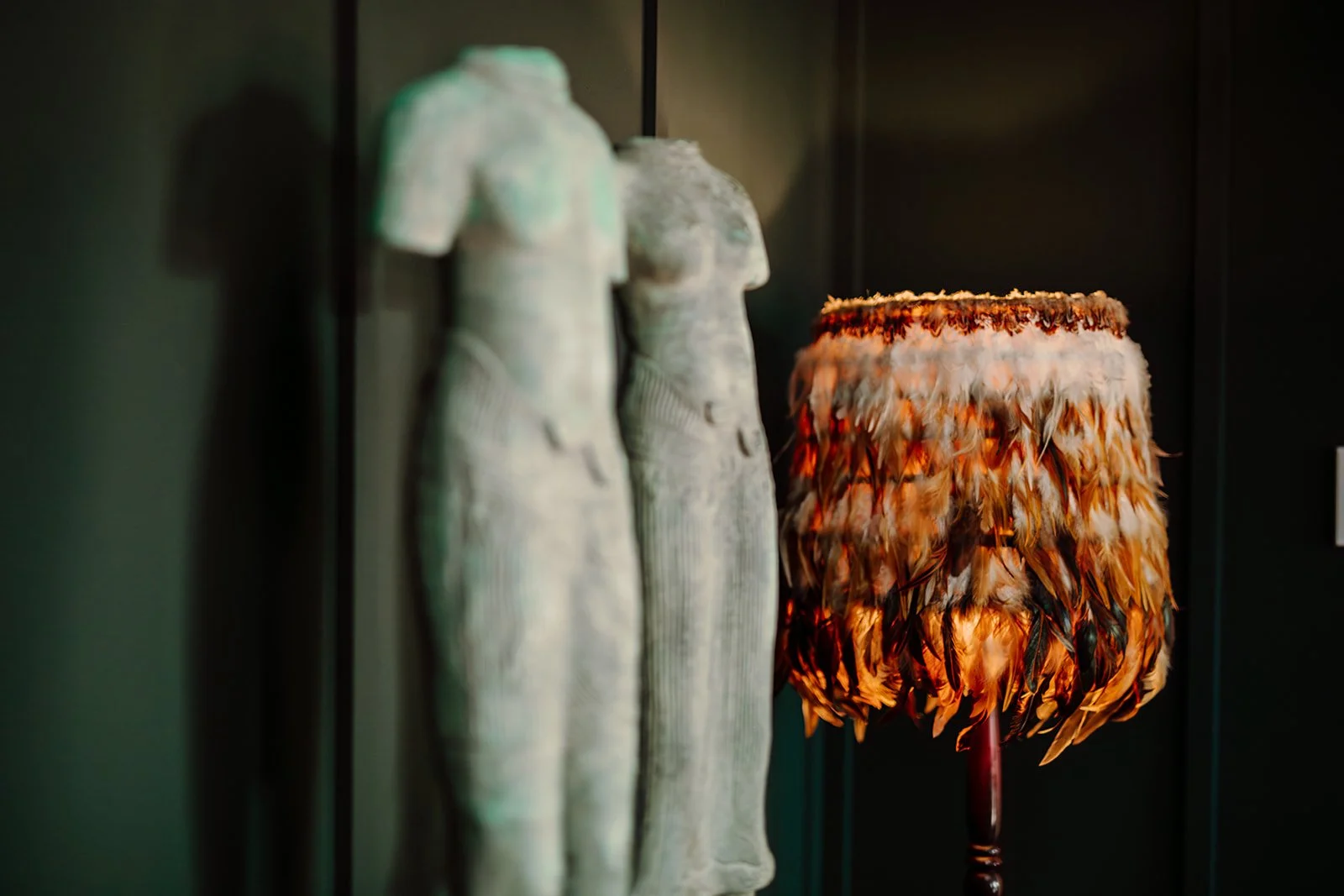 Two ancient stone statues of female figures and a floor lamp with a shade decorated with bird feathers.