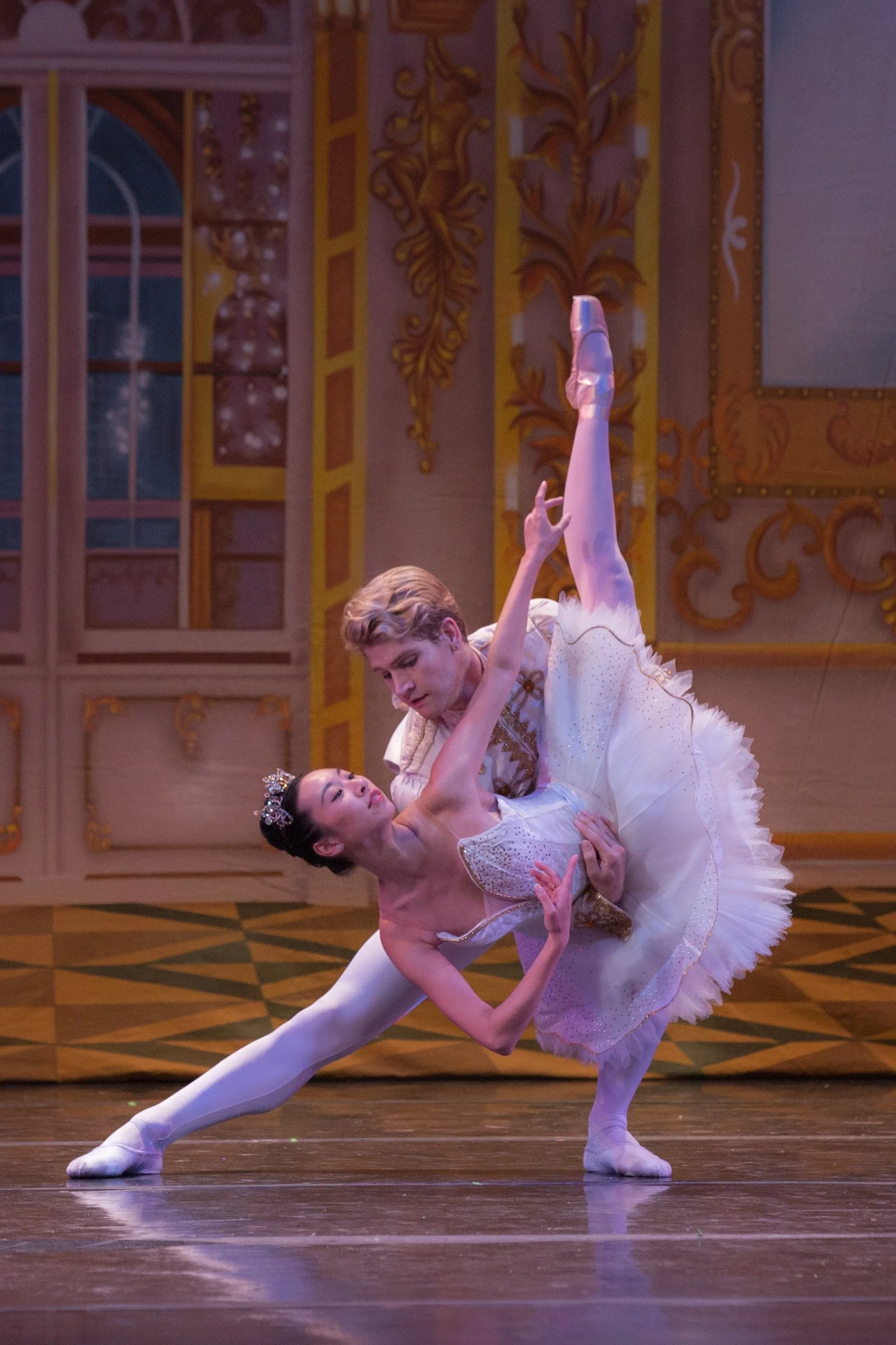 Two ballet dancers performing a lift on stage with ornate, classical set design in the background.