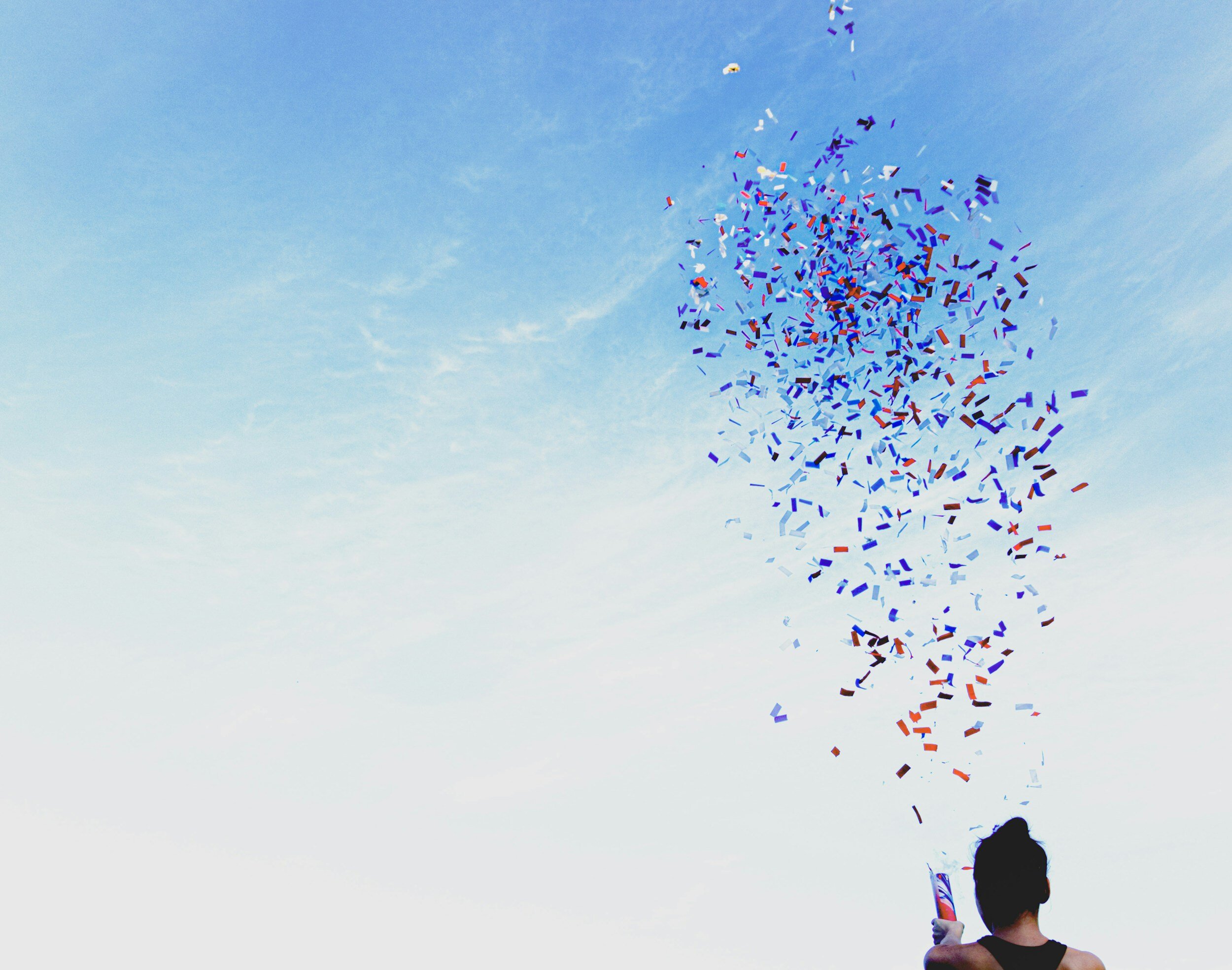 Person releasing confetti into a bright blue sky.