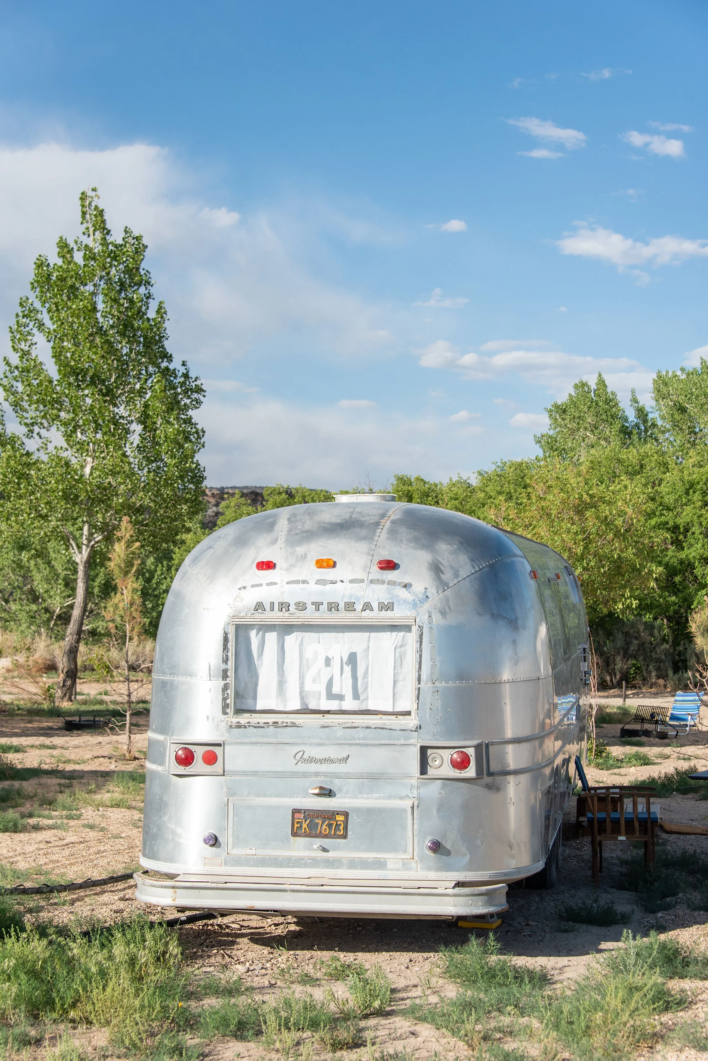 A vintage Airstream camper trailer parked outdoors with trees and a blue sky in the background.