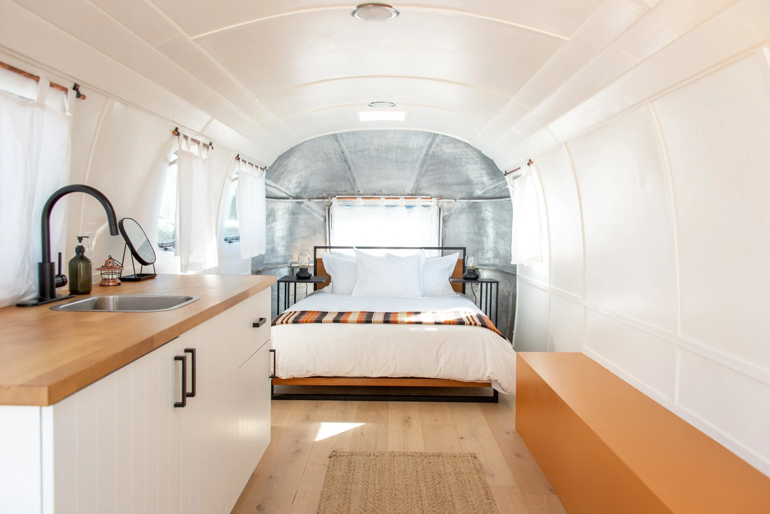 Vintage Airstream - Interior of an Airstream trailer home with a bed, small kitchen sink, and a wood bench along the wall.