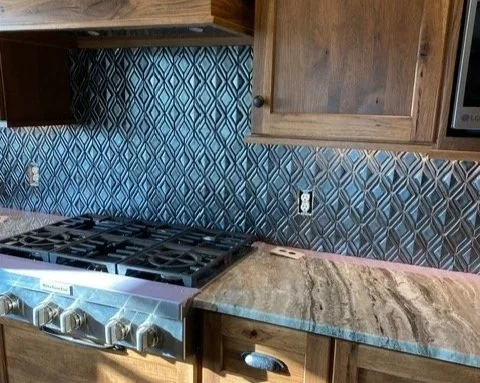 Remodeled kitchen countertop with a stove and a wooden cabinet above, patterned tile backsplash in blue and gray.