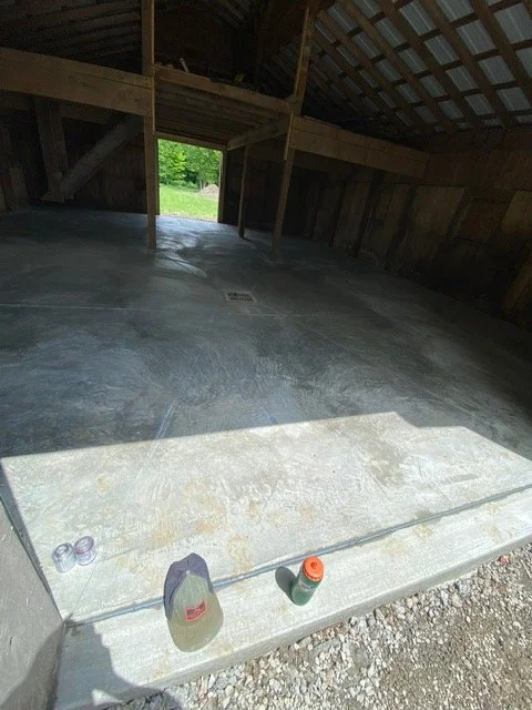 Newly poured concrete floor, wooden walls and roof, and an open door leading outside