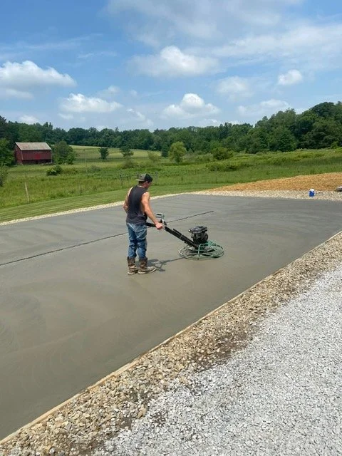 A man operating a plate compactor on freshly poured concrete to level it