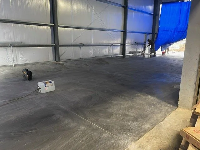 Two workers are preparing the concrete floor inside a building under construction