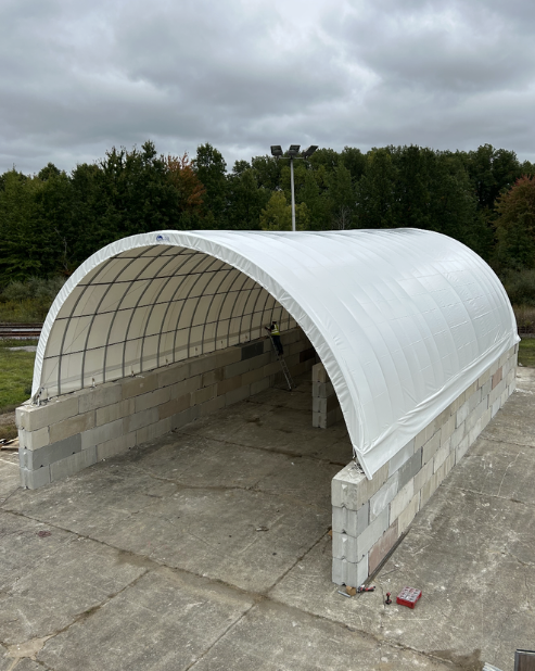 A partially constructed outdoor structure with a curved white roof supported by cinder blocks situated on a concrete surface