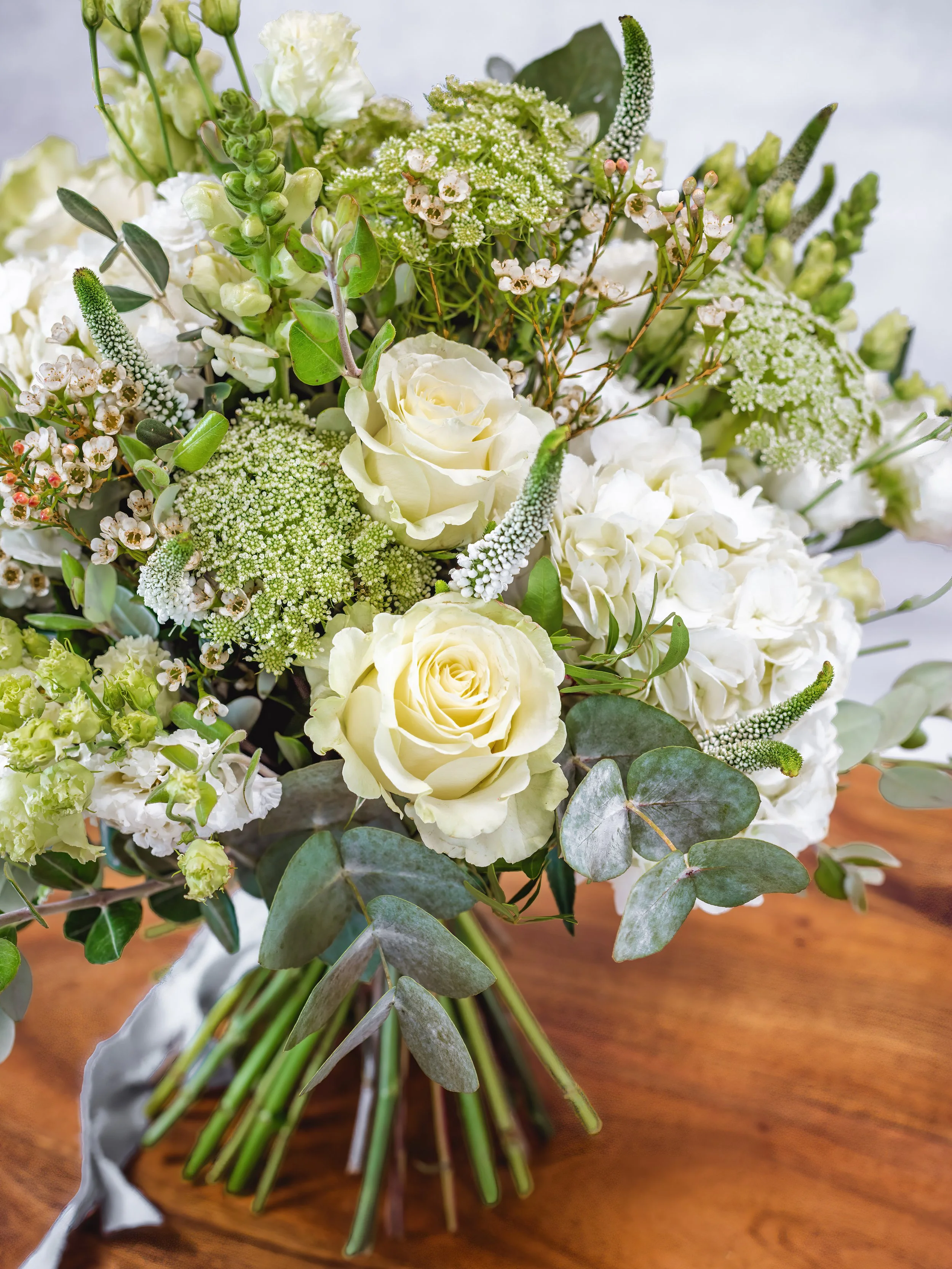 A bouquet of white and green flowers including roses and other floral varieties on a wooden surface.