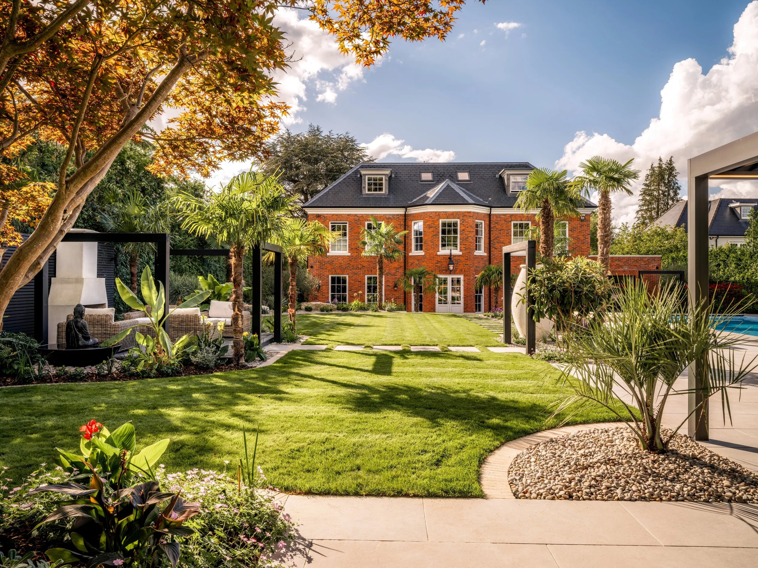 Californian-inspired garden in Surrey with palms, contemporary pergolas and formal lawn leading to red brick house