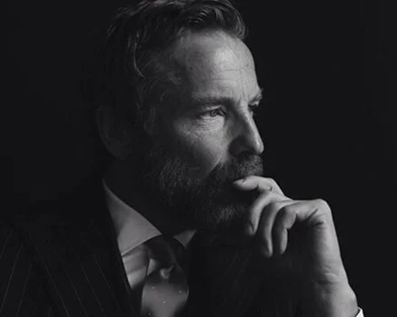 Black and white portrait of a man with a beard, looking thoughtful with his hand on his chin.