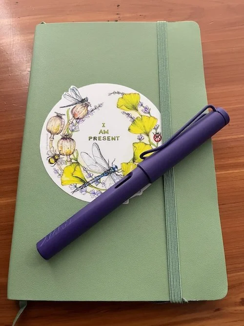 Notebook with a sticker on it and a purple pen