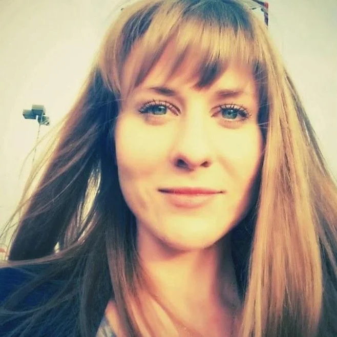 Justine Fraser, a woman with long light brown hair and bangs, smiling softly.