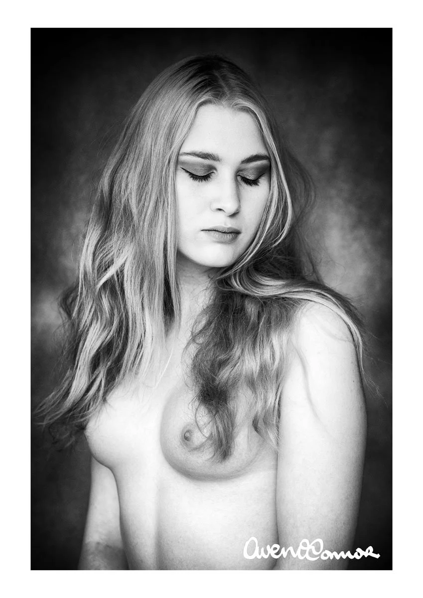 Black and white portrait of a young woman with long wavy hair, eyes closed, and a serene expression, with no clothing visible except for her bare shoulder.