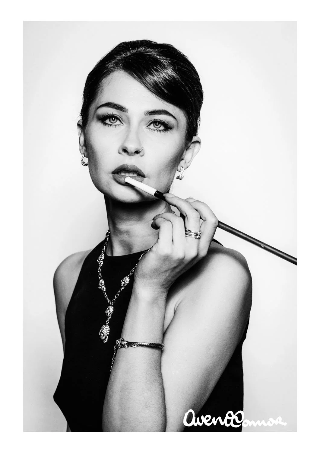 A black and white portrait of a woman with short hair, jewelry, and a sleeveless top, holding a cigarette holder near her lips, with a sign that reads 'AwenO' in the bottom right corner.