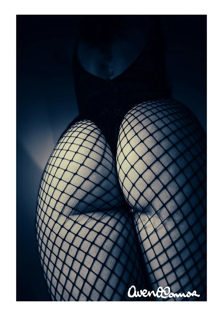 Close-up of a person's legs wearing fishnet stockings, with a signature at the bottom right corner.