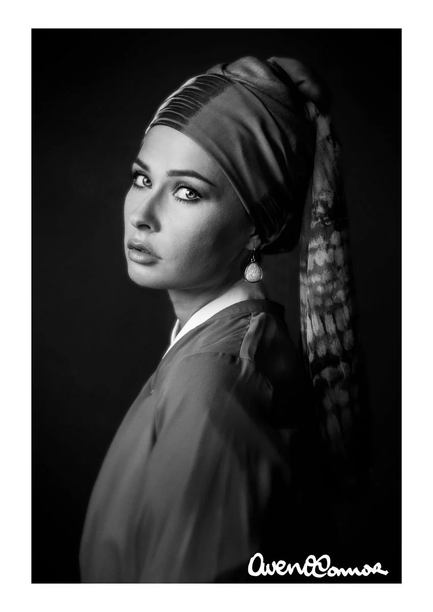 Black and white portrait of a woman wearing a headscarf and earrings, looking over her shoulder with a serious expression.