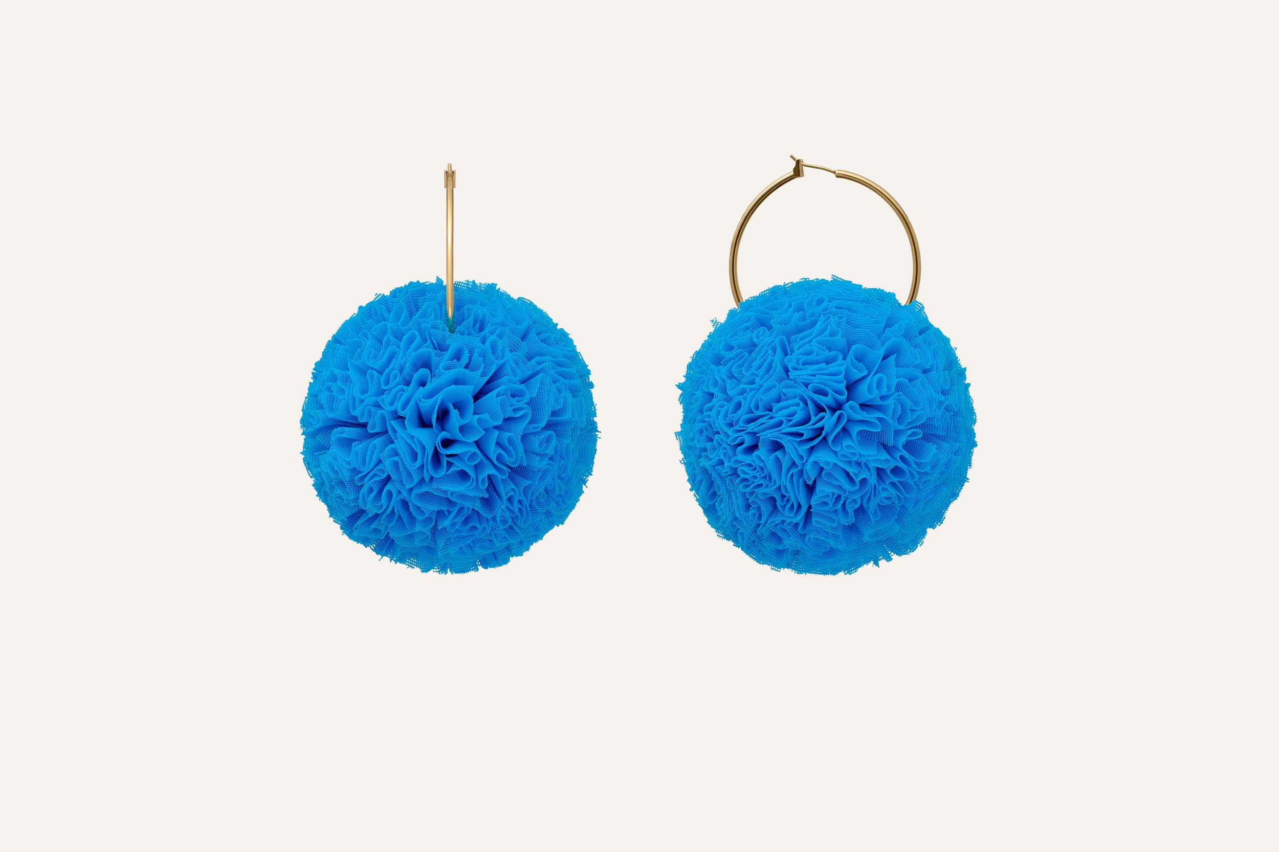 A pair of blue pom-pom earrings with gold hoops on a light background.  Jewellery packshot photography