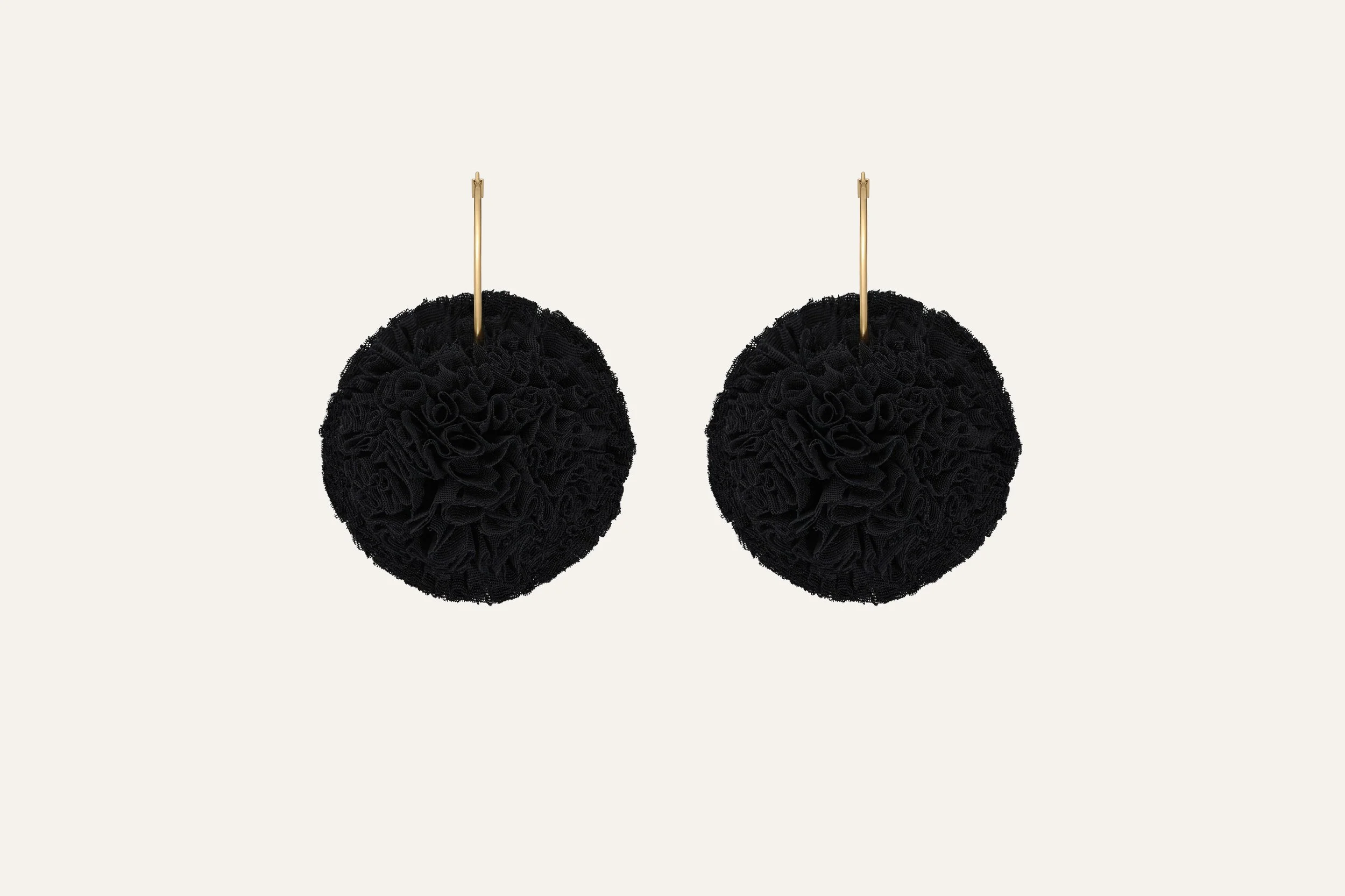 Black, textured, round earrings with gold hooks hanging against a light background. Jewellery packshot