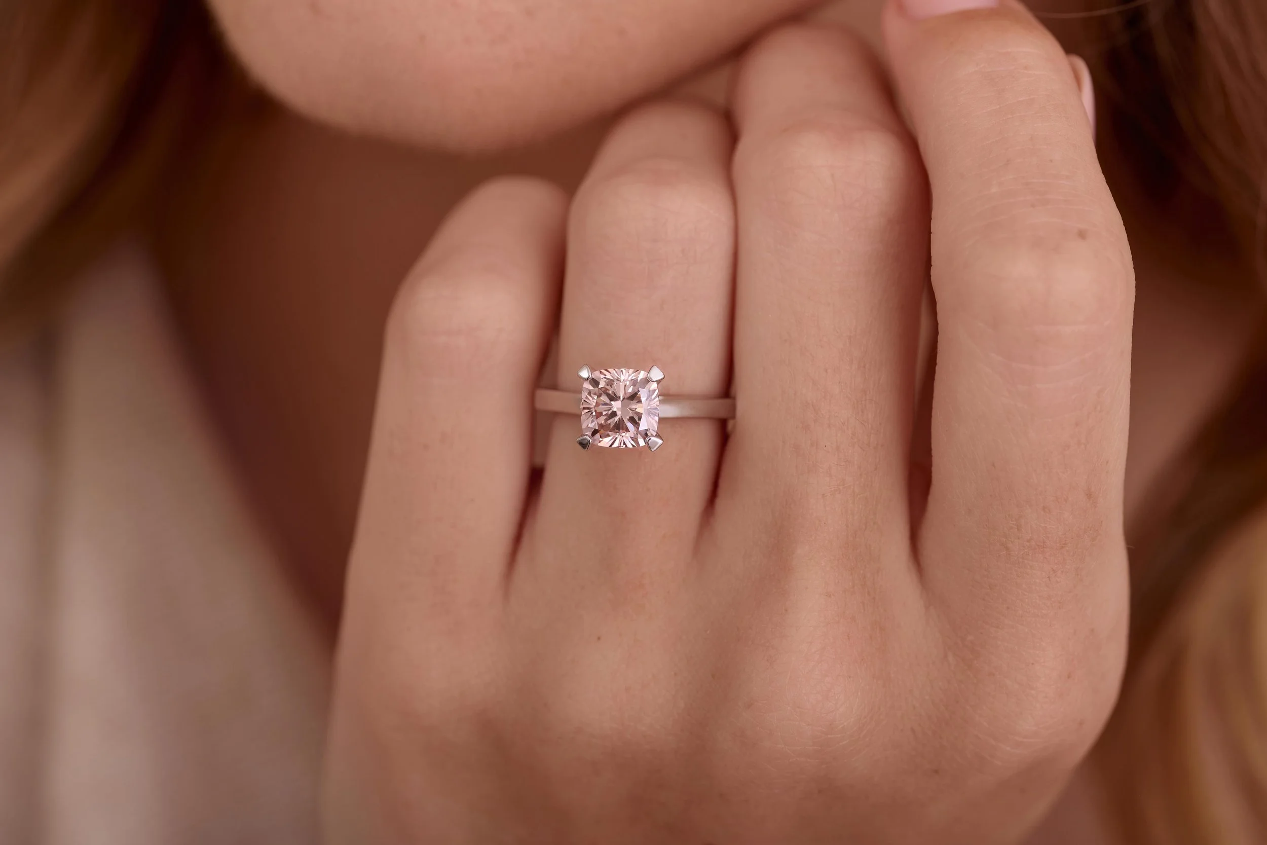 Close-up of a woman's hand wearing an engagement ring with a pink gemstone, near her lips. Jewellry on model photography in London