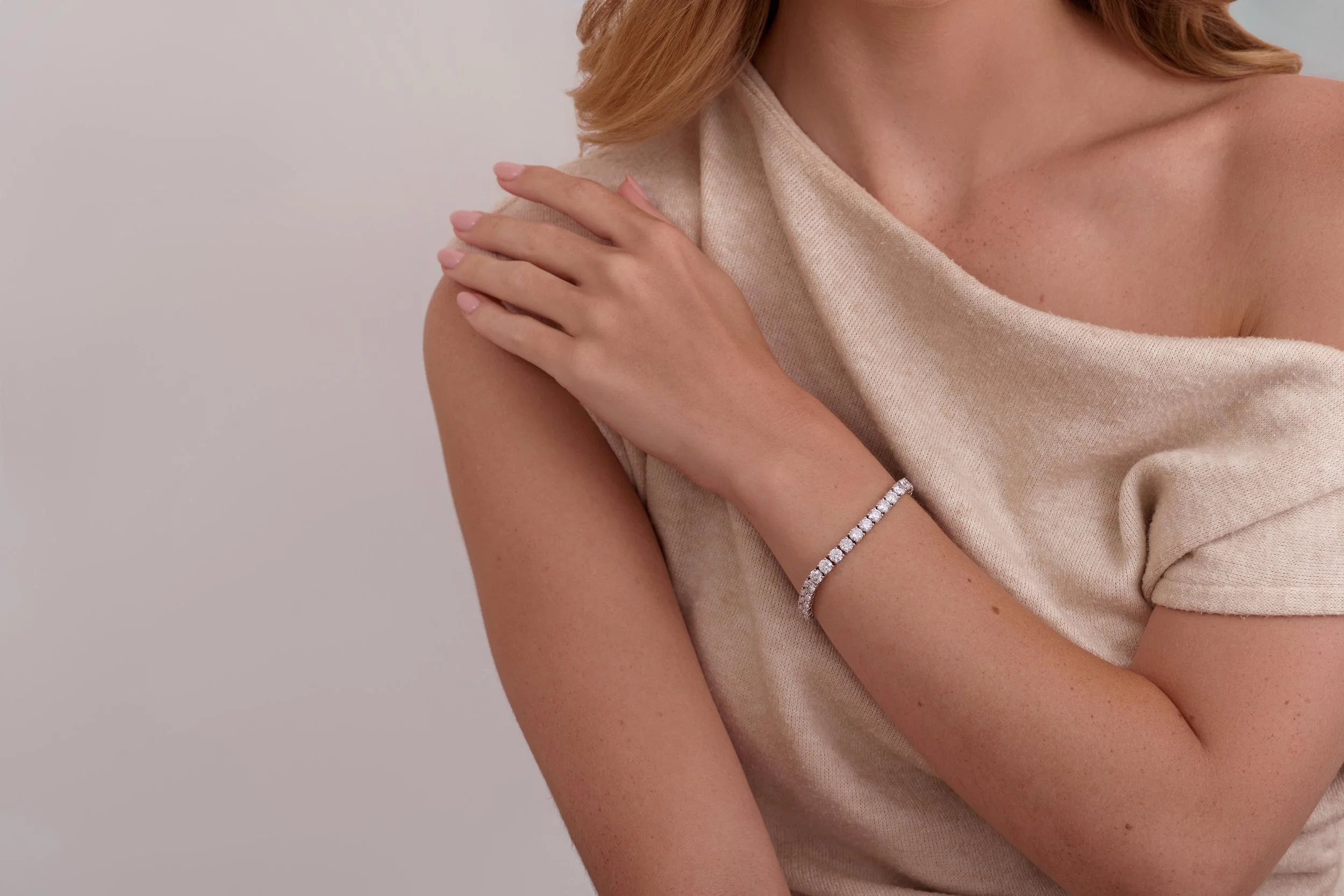 A woman wearing a beige top, with one hand resting on her shoulder, showing a diamond bracelet on her wrist. Jewellry on model photography in London