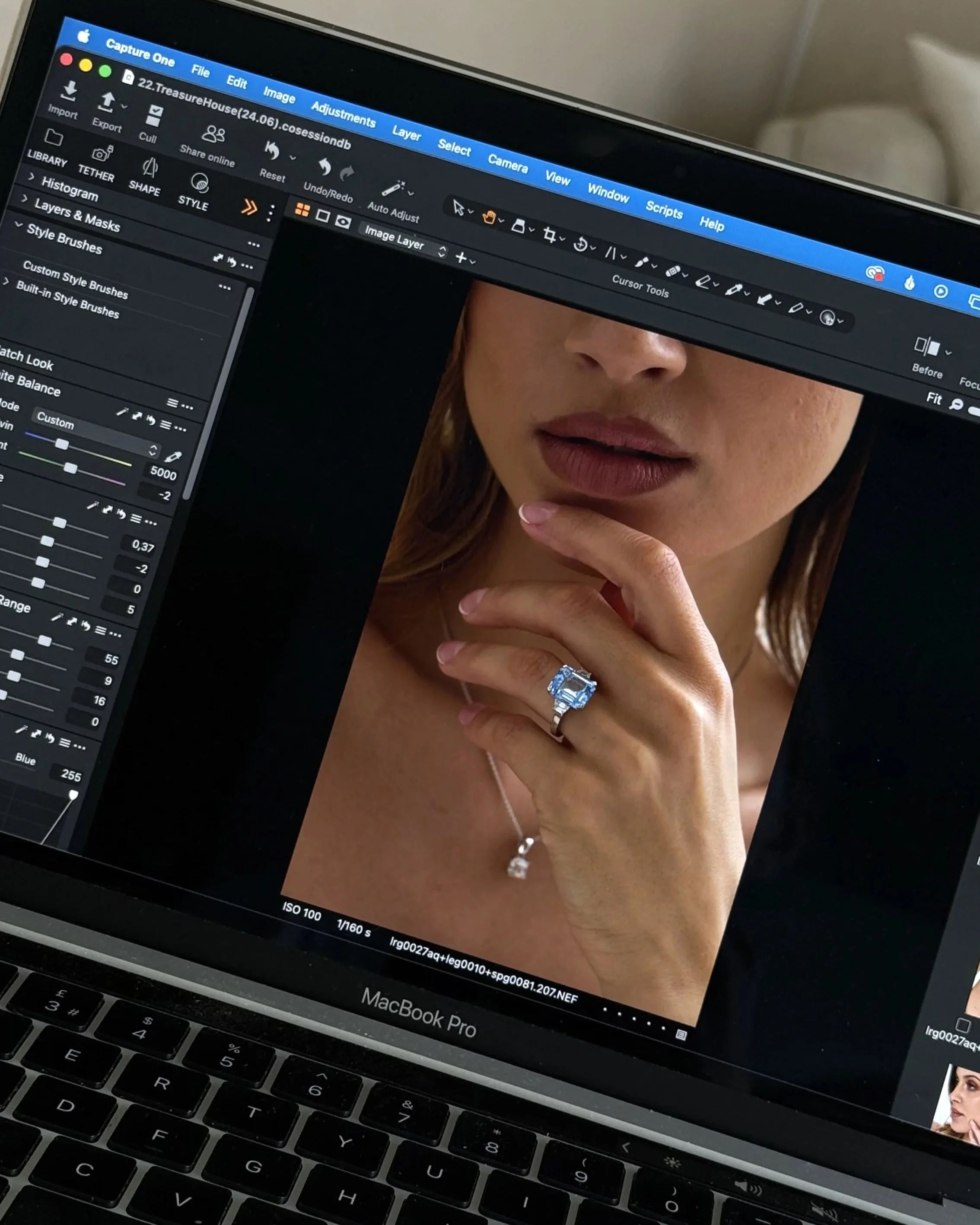 Close-up of a laptop screen displaying photo editing software with an edited photo of a woman's face and jewelry, including a ring and necklace, along with various editing controls and tools visible on the screen.