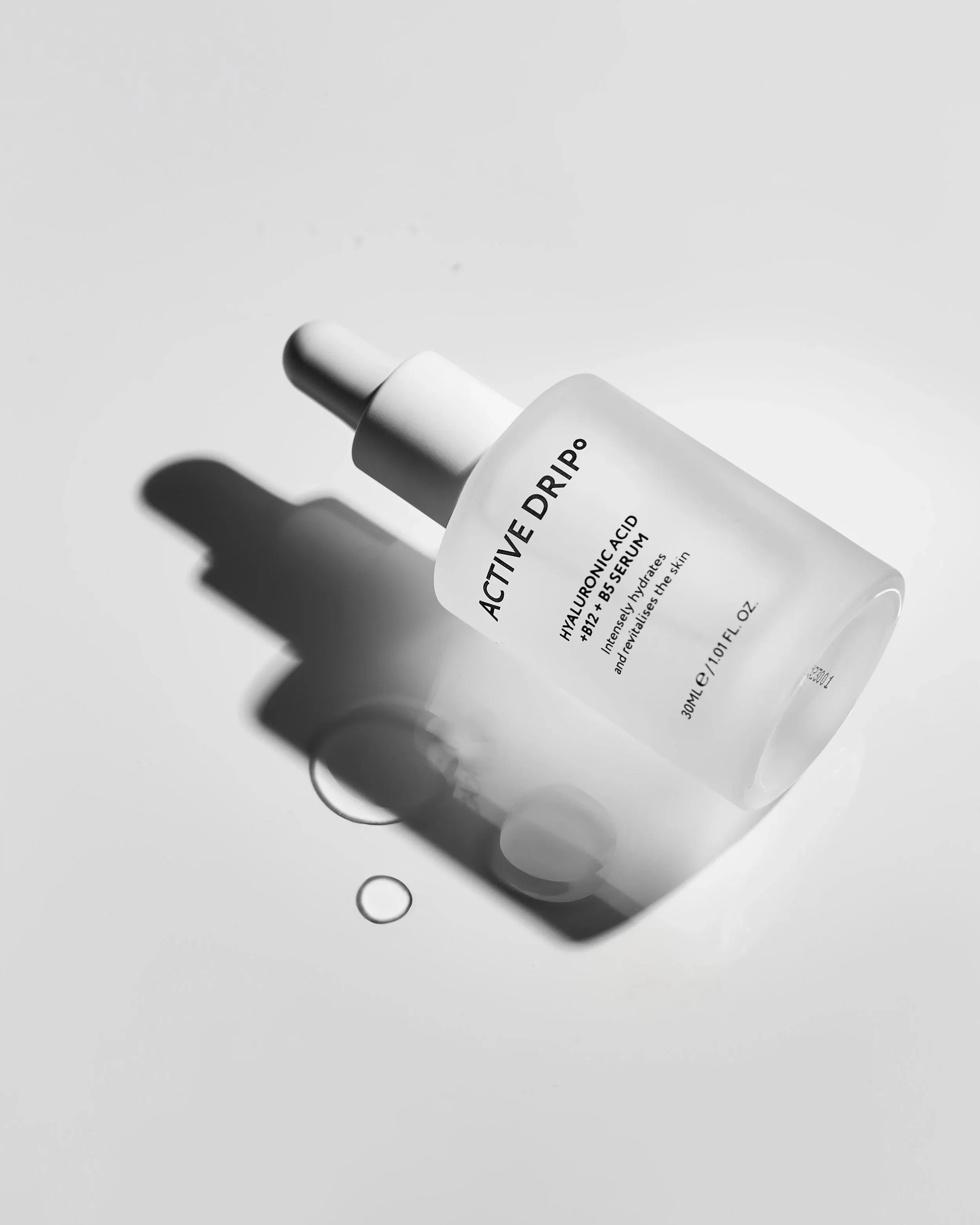 Close-up of a skincare serum bottle labeled 'ACTIVE DRIP' with a drop of serum below it, on a plain grey backdrop, product photography