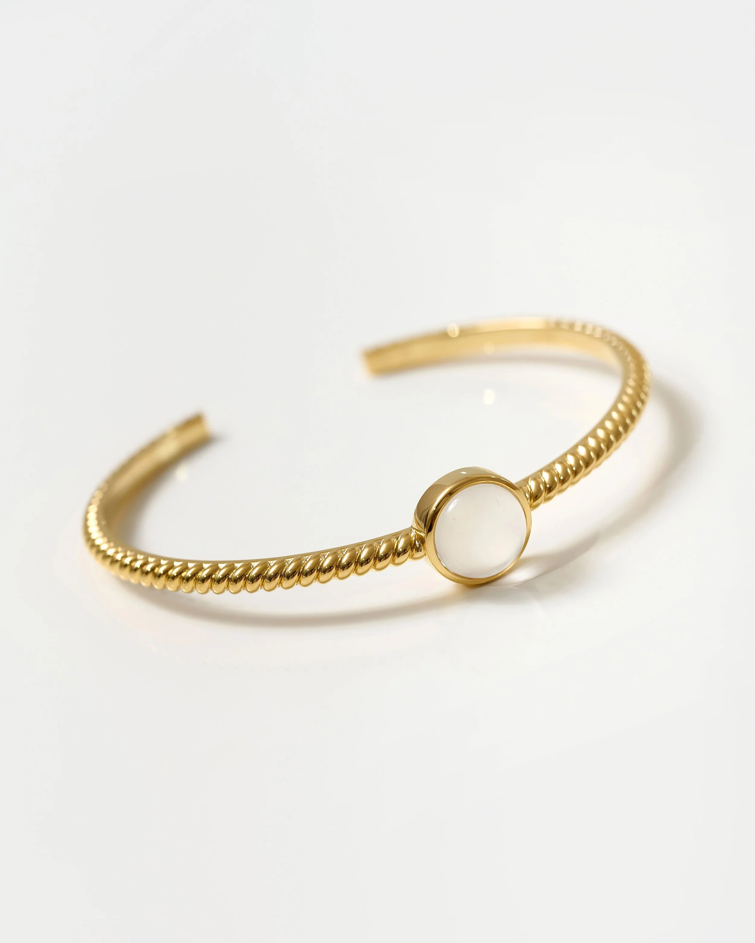 Close-up of a gold bracelet with a circular white stone on a white background.  Jewellery packshot photography