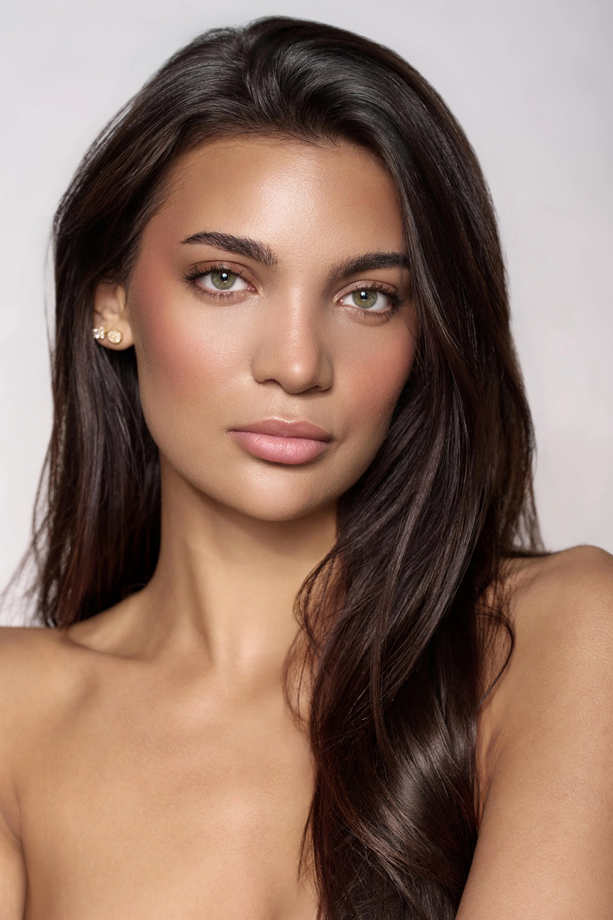 Close-up of a model with long dark hair and light makeup, looking directly at the camera against a plain background. Natural beauty portrait in London