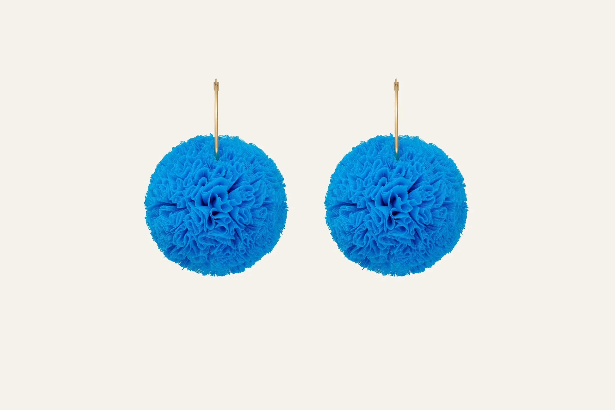 Two blue bath sponges with absorbent mesh texture hanging on gold hooks against a plain white background.  Jewellery packshot photography