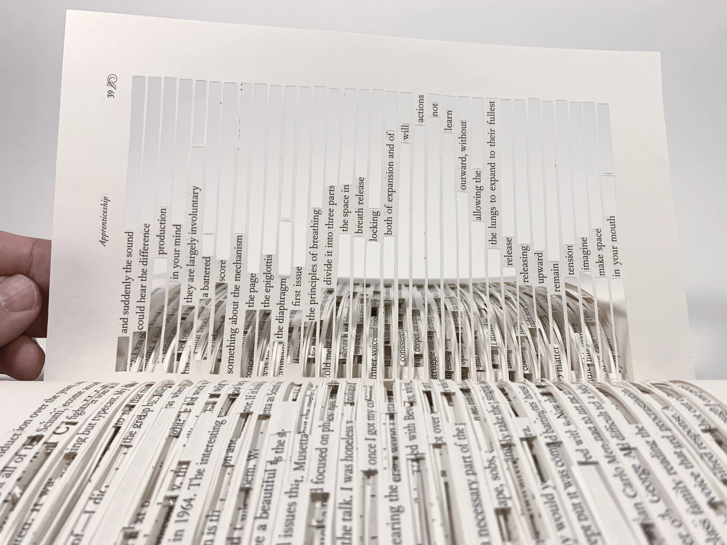 Close up of a page from the Dissection book, where most lines and words have been cut out, leaving a snake of words down over the page, containing a found poem by Autistic Artist and Architect Troels Steenholdt Heiredal