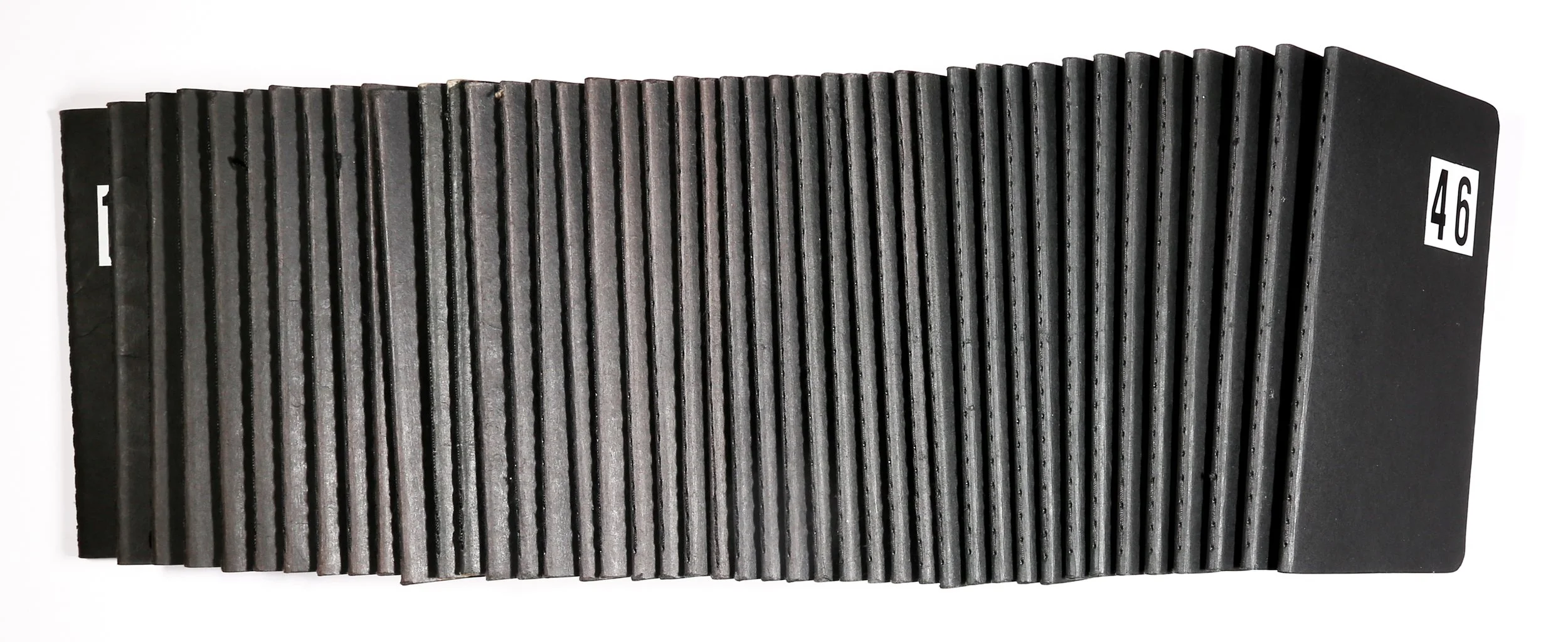 Photograph of the black Moleskine textures notebooks. On the first book, the edge of the number 1 is visible and the last book has 46 on the cover.
